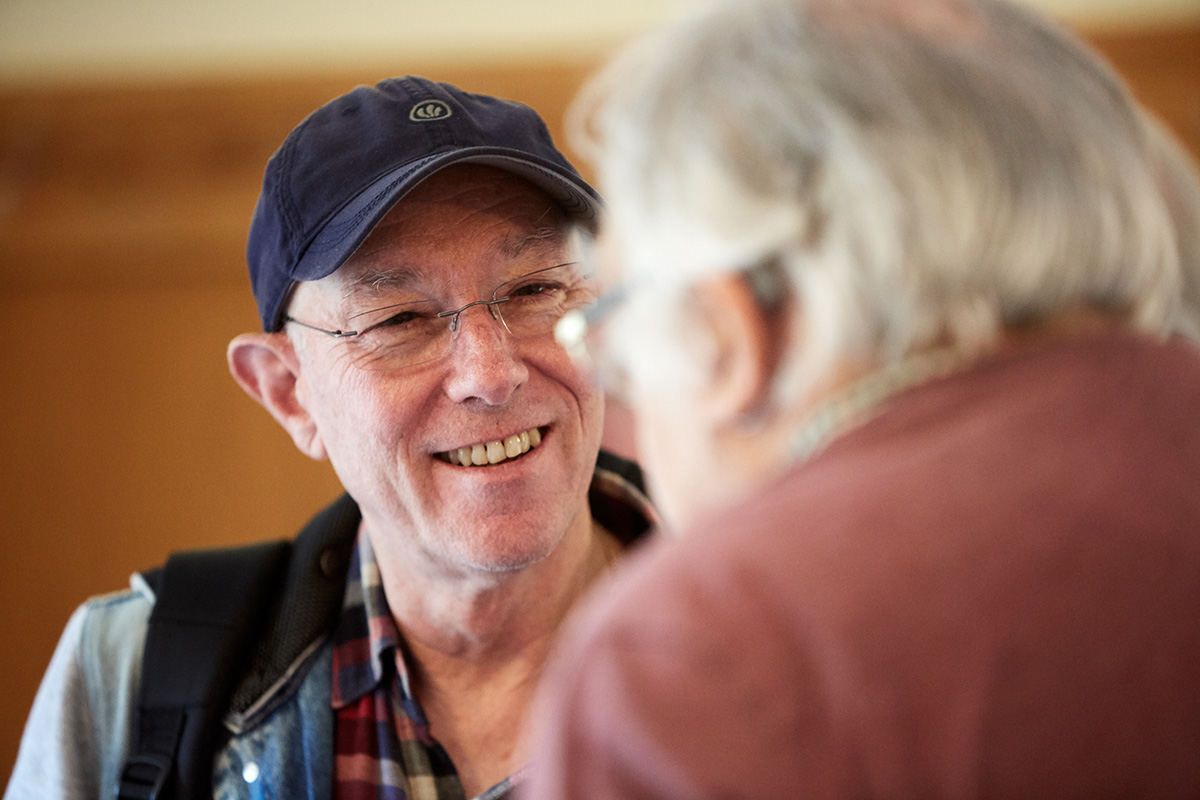 Two men chatting, one facing the camera is smiling warmly.