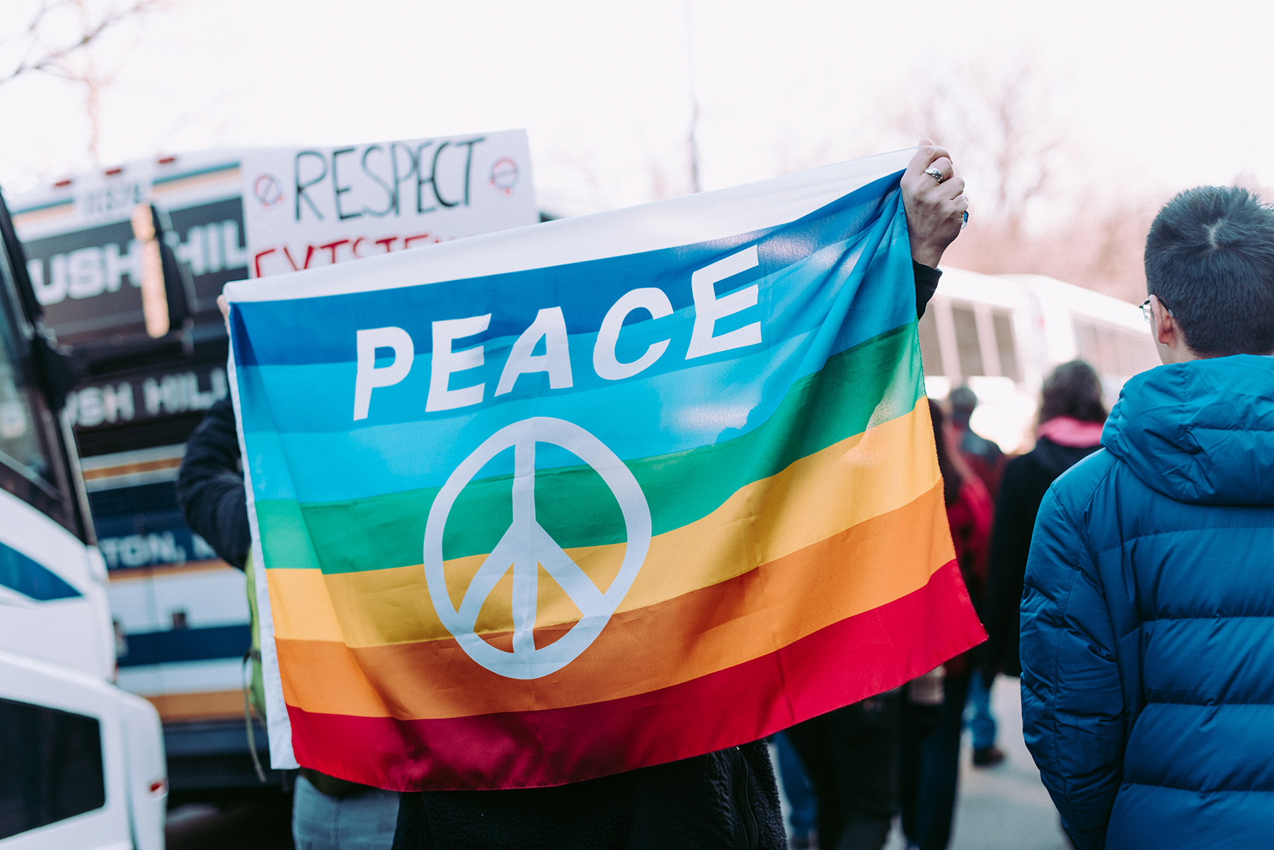 A rainbow flag reading 'Peace' is held up at a protest