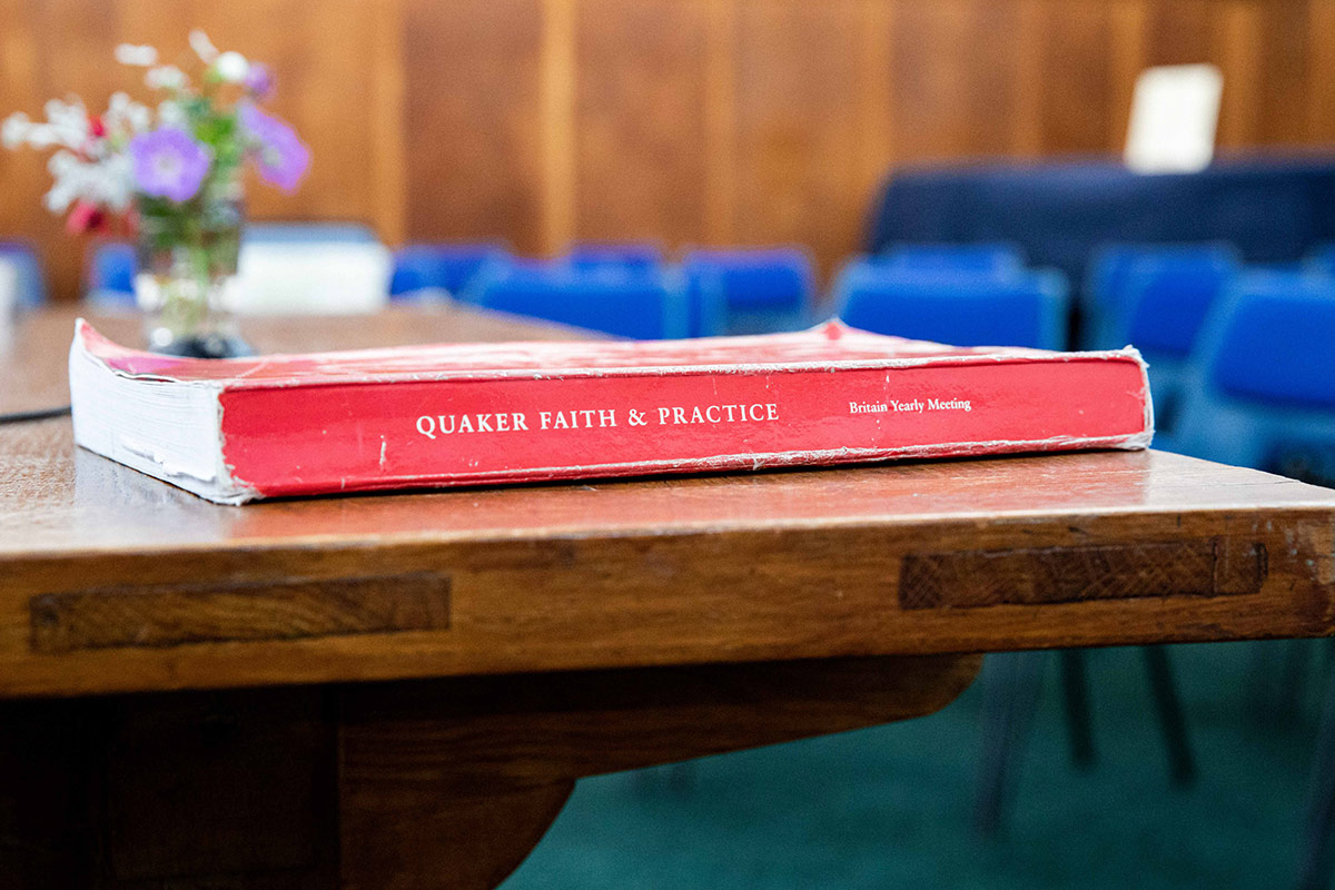 A copy of the book 'Quaker Faith & Practice' lies on a table with flowers in the background
